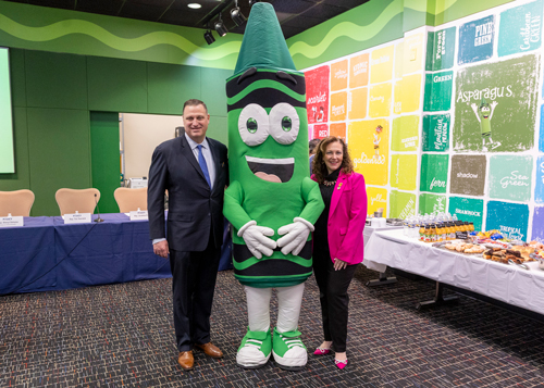Rep. Ann Flood (R-Northampton) shares a moment with Pete Ruggiero, president and CEO of Crayola and the green crayon mascot at Crayola headquarters in Easton. 